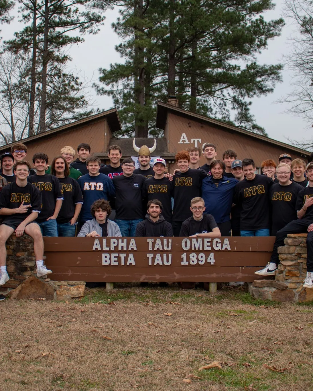 The Beta Tau chapter standing in front of the lodge sign reading "Alpha Tau Omega, Beta Tau 1894"