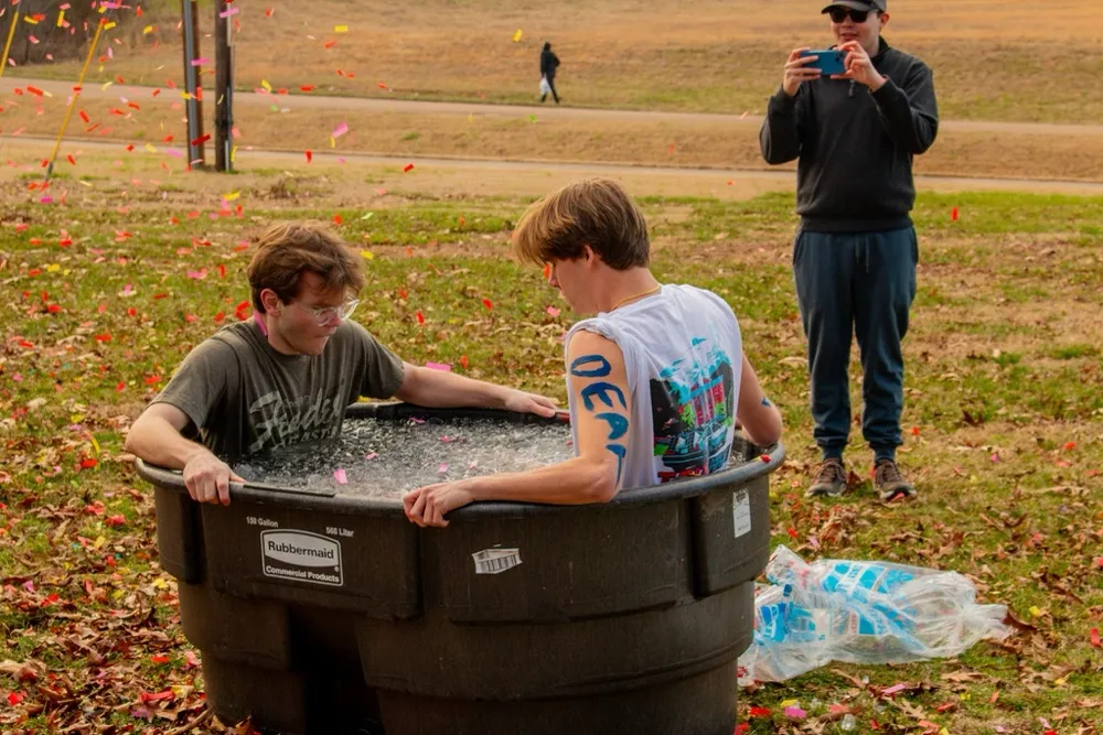 Two brothers in a tub of ice water for the Ice Bath Challenge fundraiser, confetti in the air, a brother filming on his phone