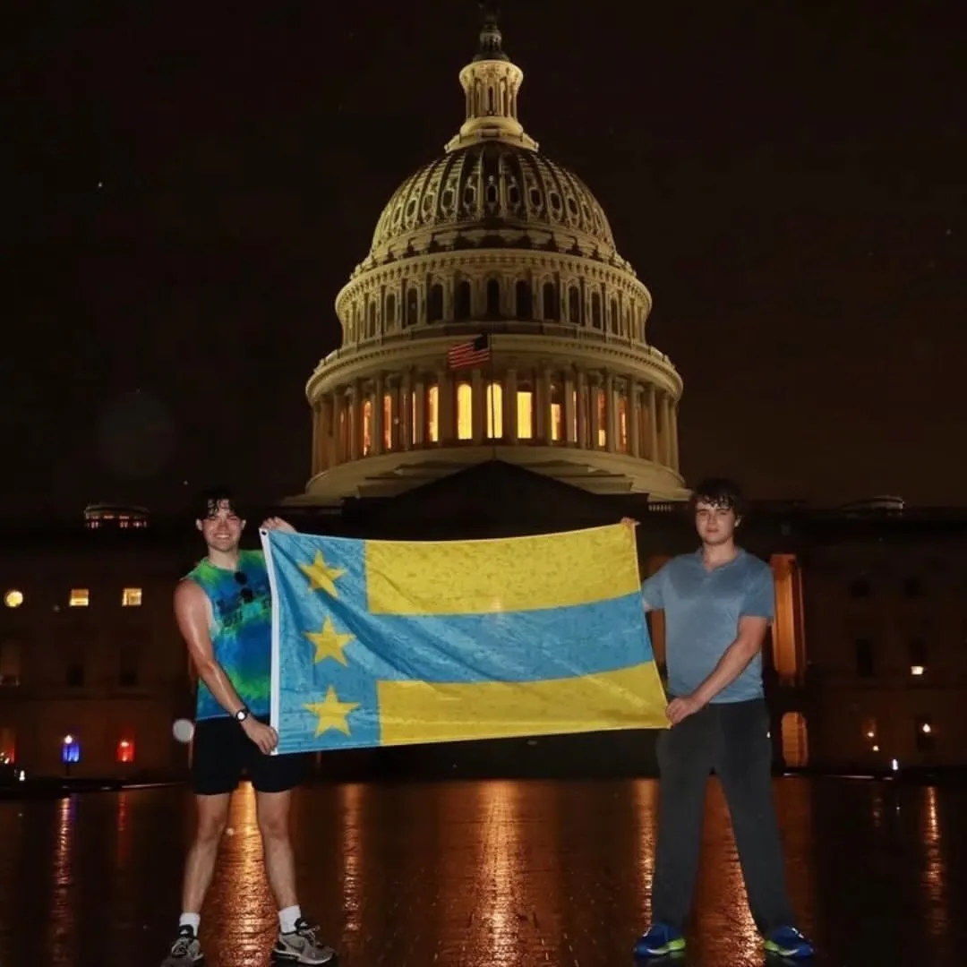 Two brothers holding a flag at night in front of the U.S. Capitol
